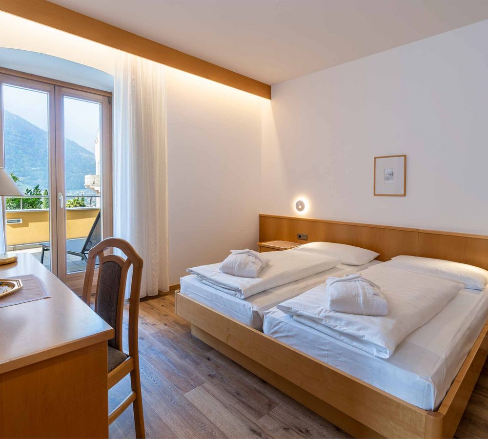 Helles, modernes Hotelzimmer mit zwei Einzelbetten, Holzmöbeln und Balkon mit Bergblick.