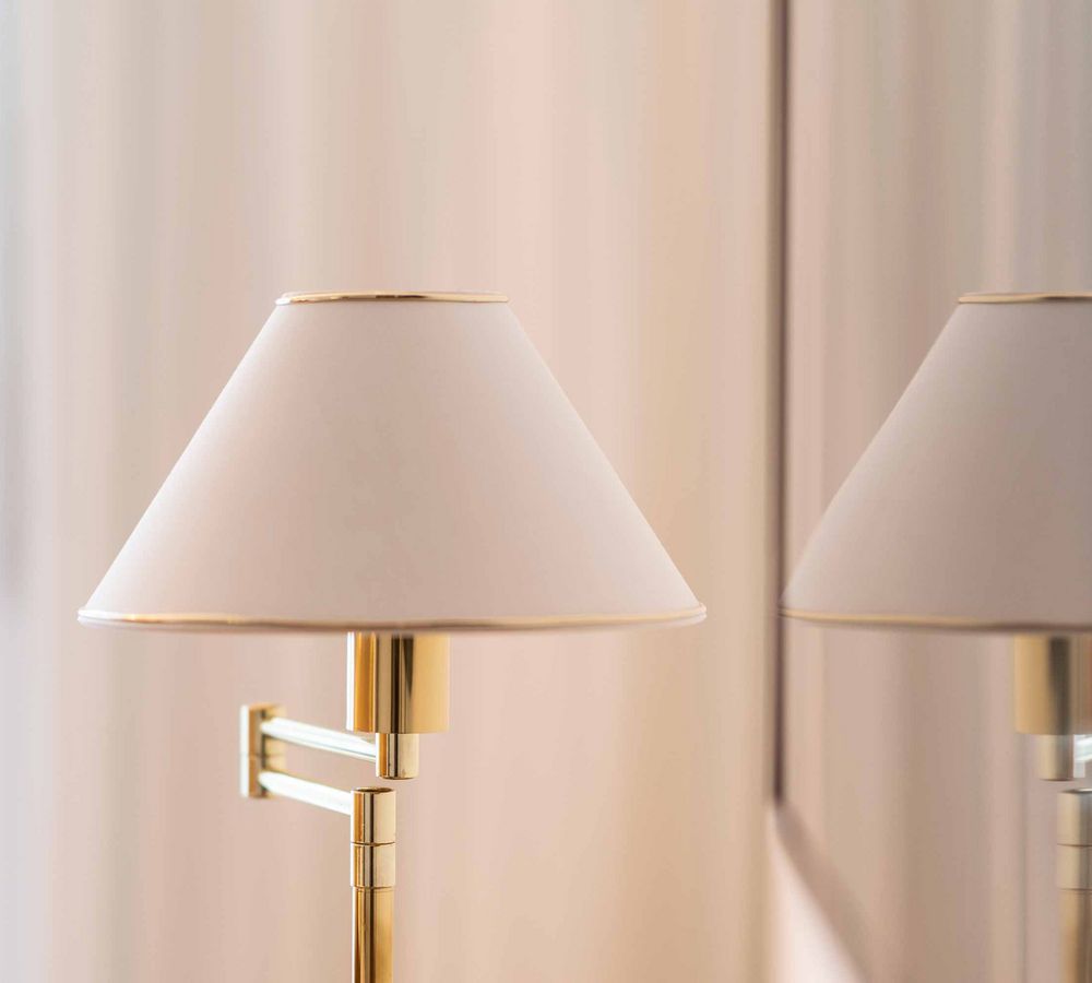 Elegante Tischlampe mit weißem Lampenschirm und goldenem Gestell vor hellem Hintergrund und Spiegelung