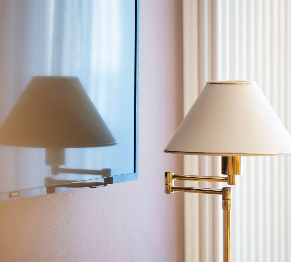 Beige Stehlampe mit Metallarm vor einem Fernseher, der die Lampe reflektiert.