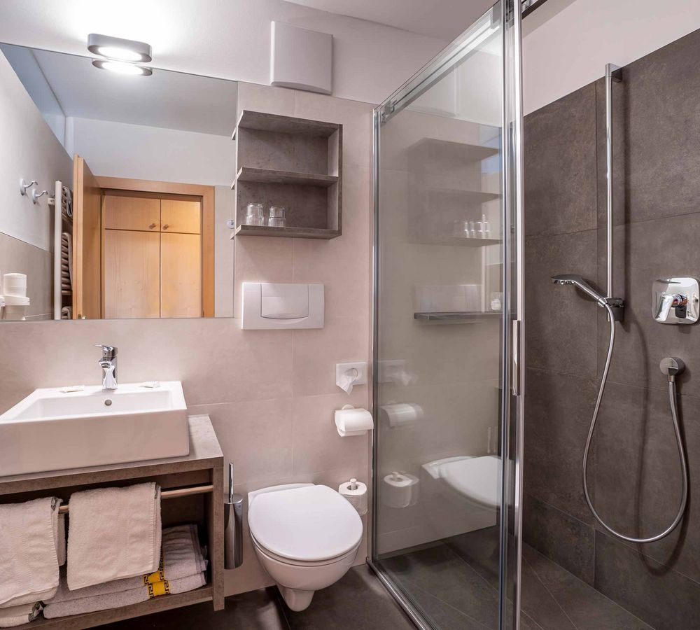 Modernes Bad mit Waschbecken, Toilette, Dusche mit Glastür und grauen Fliesen