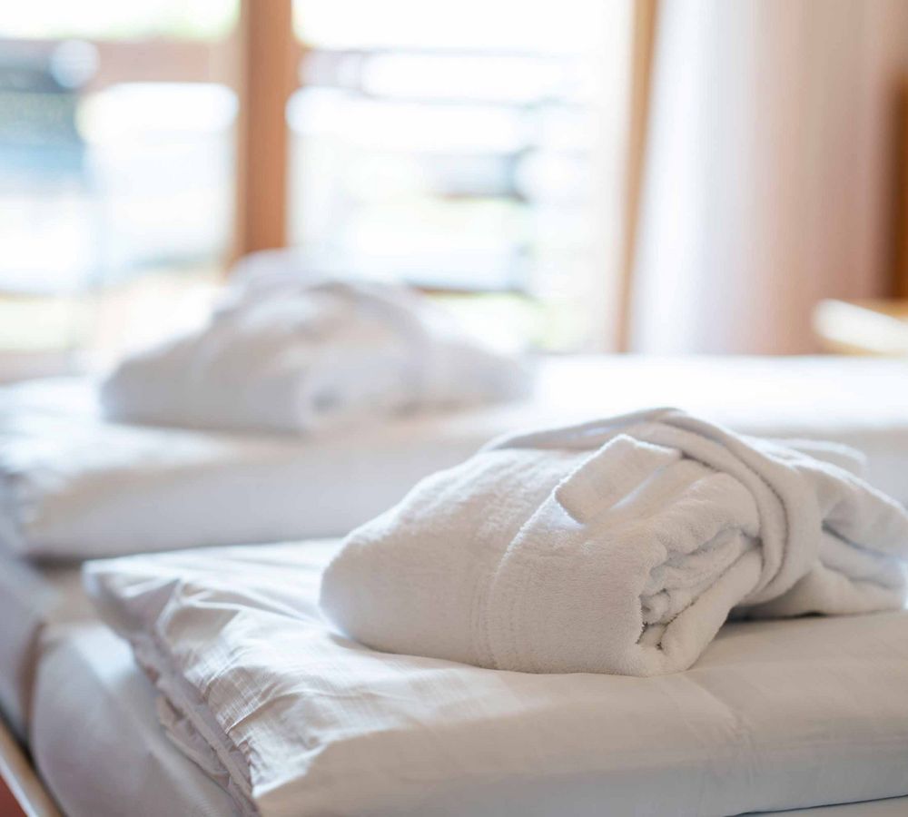 Weißer Bademantel auf einem gemütlich gemachten Bett in einem hellen Hotelzimmer