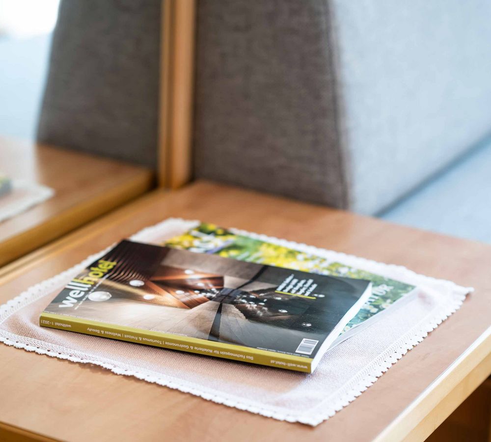 Ein Magazin mit dem Titel „Wellhotel“ liegt auf einem Holztisch neben einem grauen Sofa.