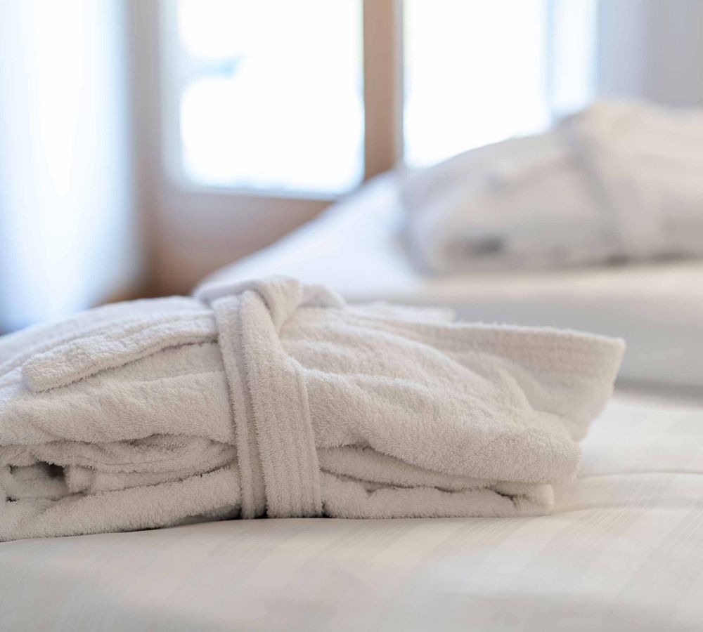 Gefaltener weißer Bademantel liegt auf einem Bett im hellen Hotelzimmer