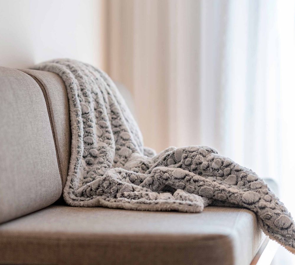 Gemütliche Decke liegt auf einem hellbraunen Sofa vor hellem Hintergrund