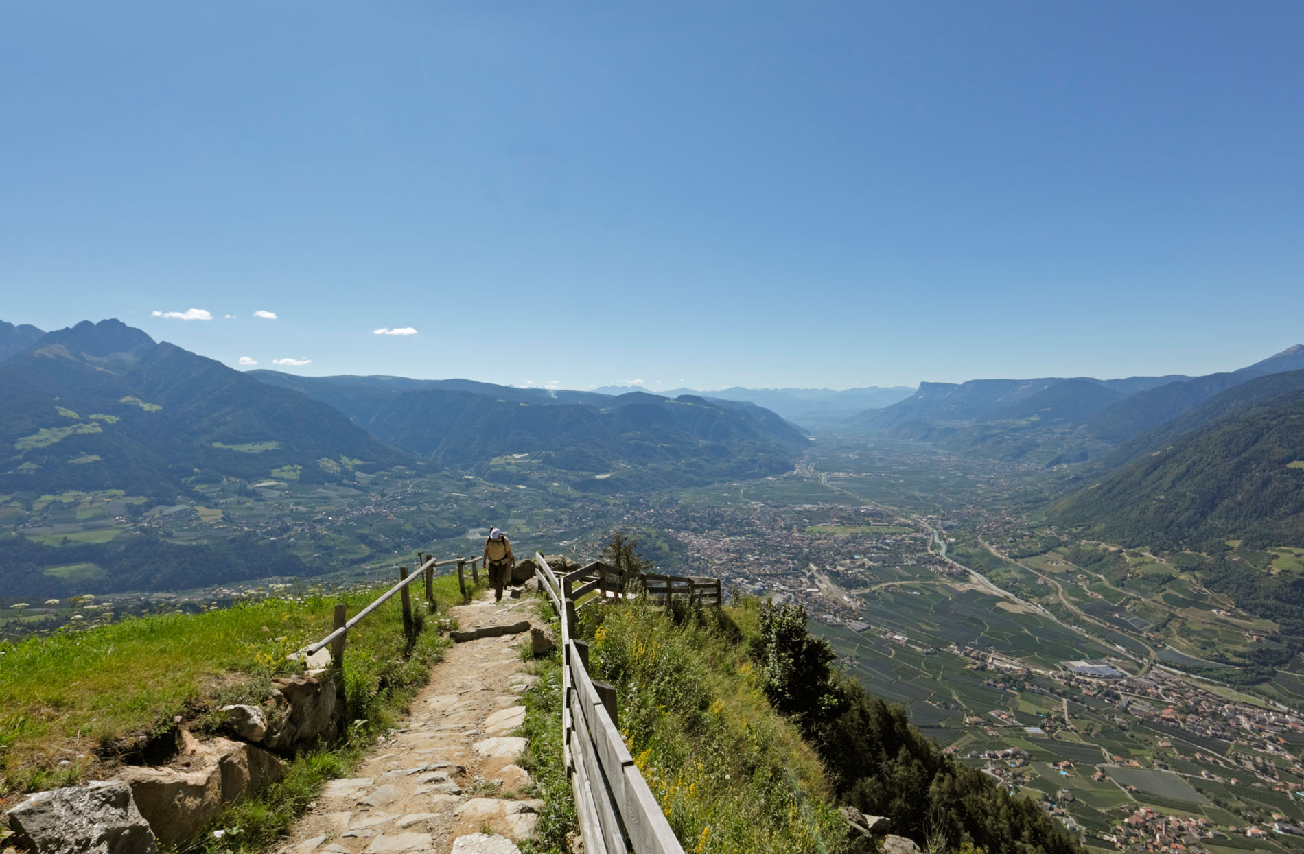 Wanderer auf felsigem Bergweg mit Tal- und Bergpanorama unter klarem blauem Himmel