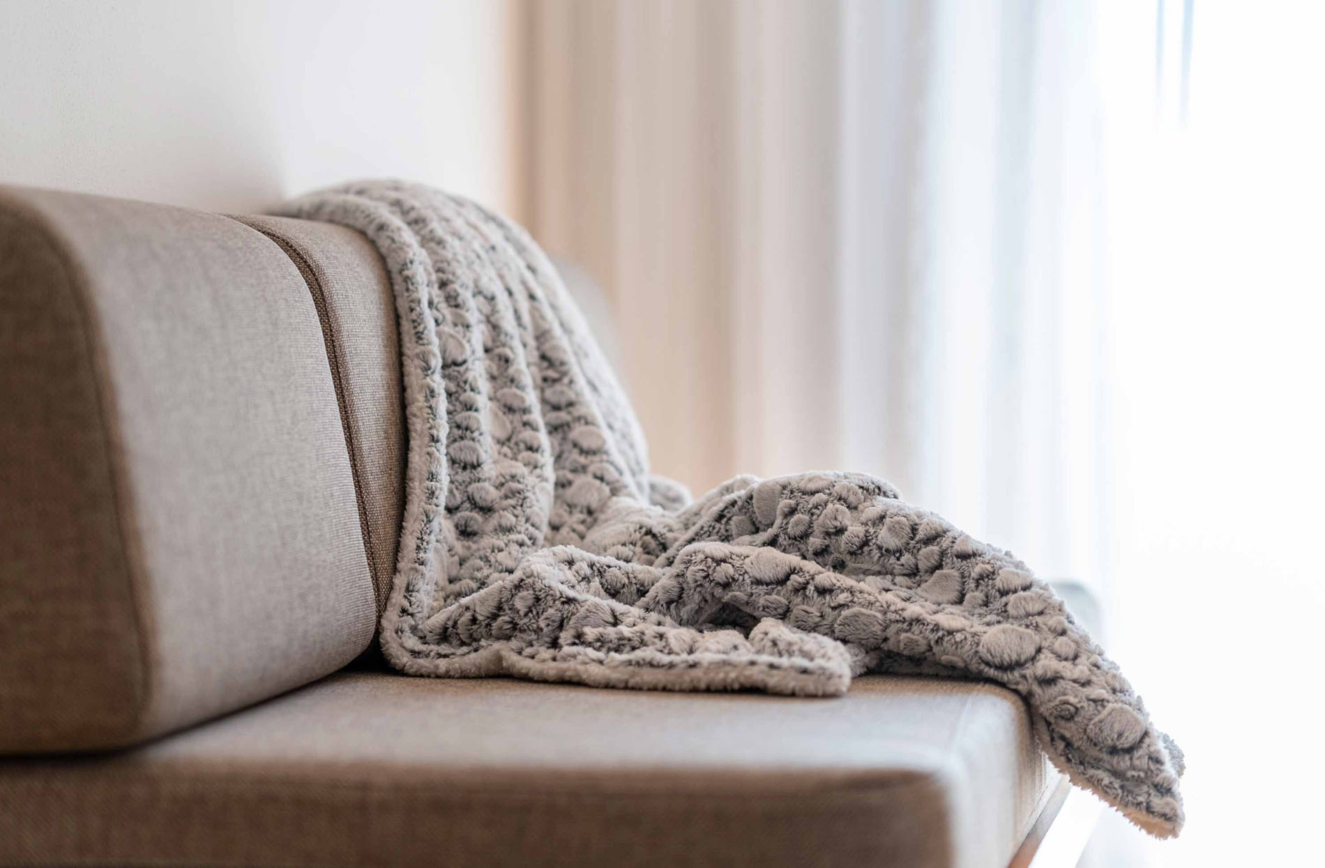 Beige Sofa mit einer weichen, grauen Decke, die lässig darauf drapiert ist. Beige Sofa mit einer weichen, grauen Decke, die lässig darauf drapiert ist.