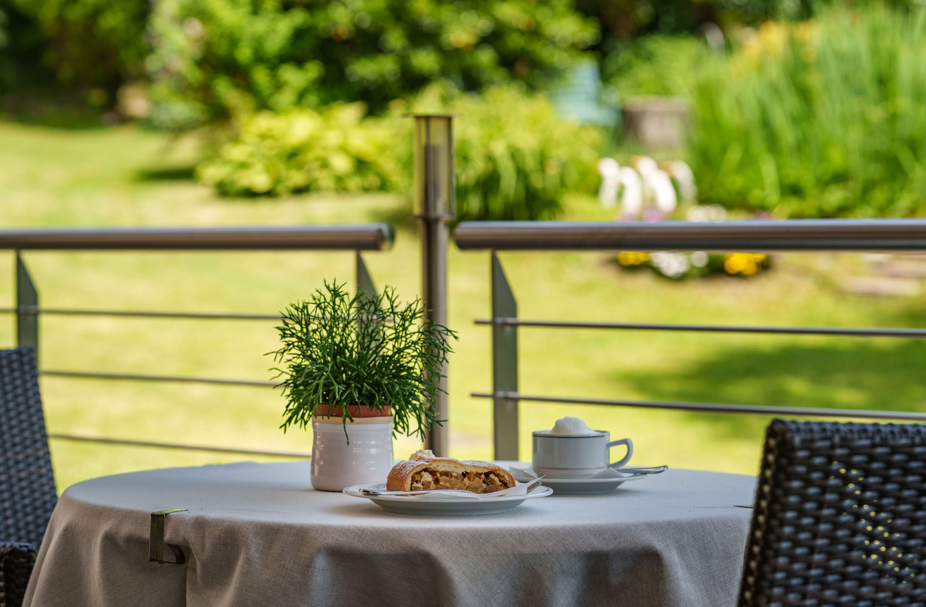 Kaffeetisch im Freien mit Kuchen, Tasse Kaffee und Topfpflanze vor grünem Garten Kaffeetisch im Freien mit Kuchen, Tasse Kaffee und Topfpflanze vor grünem Garten