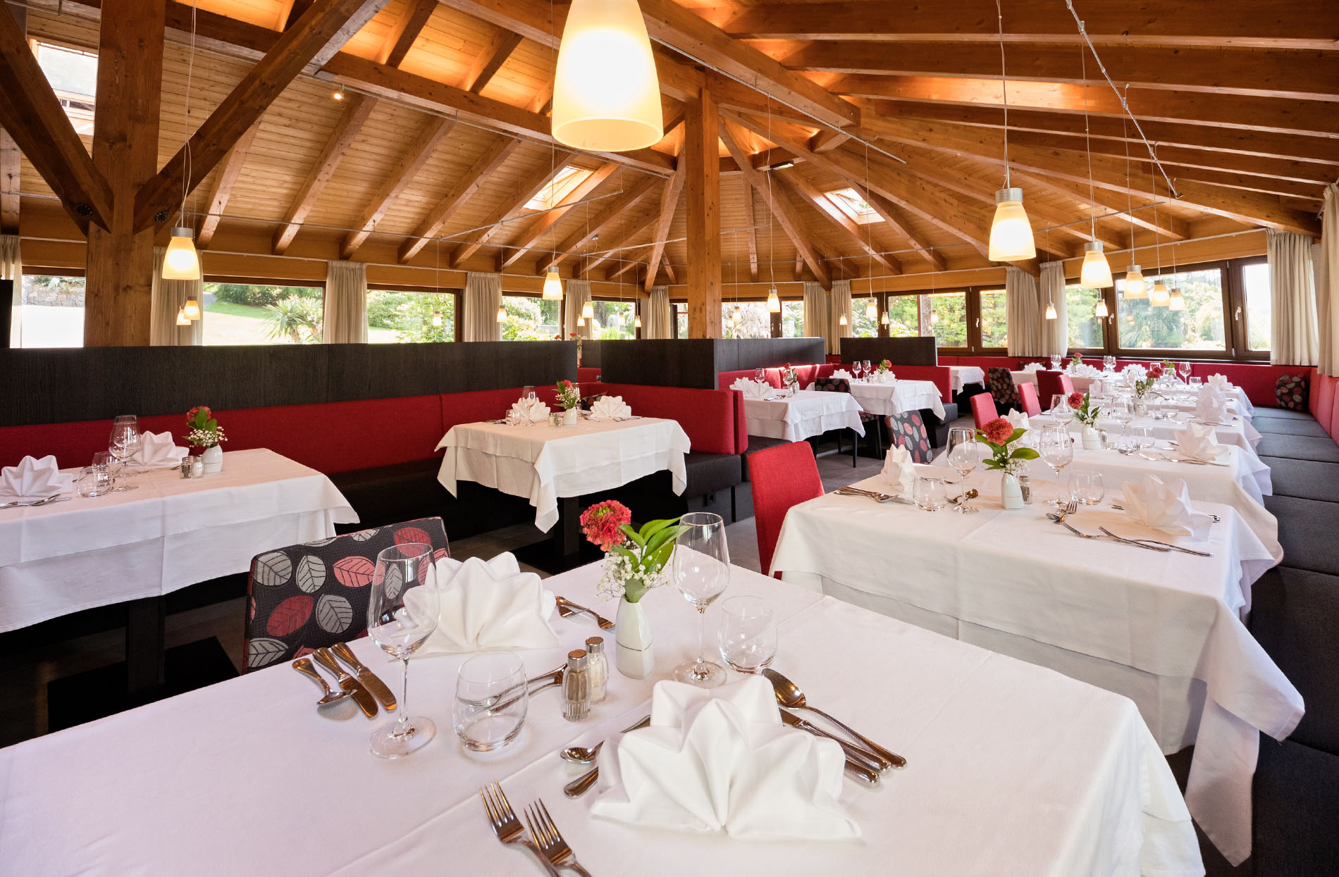 Elegantes Restaurant mit Holzdecke, rot gepolsterten Sitzbänken und gedeckten Tischen mit weißen Tischdecken und dekorierten Servietten. Elegantes Restaurant mit Holzdecke, rot gepolsterten Sitzbänken und gedeckten Tischen mit weißen Tischdecken und dekorierten Servietten.