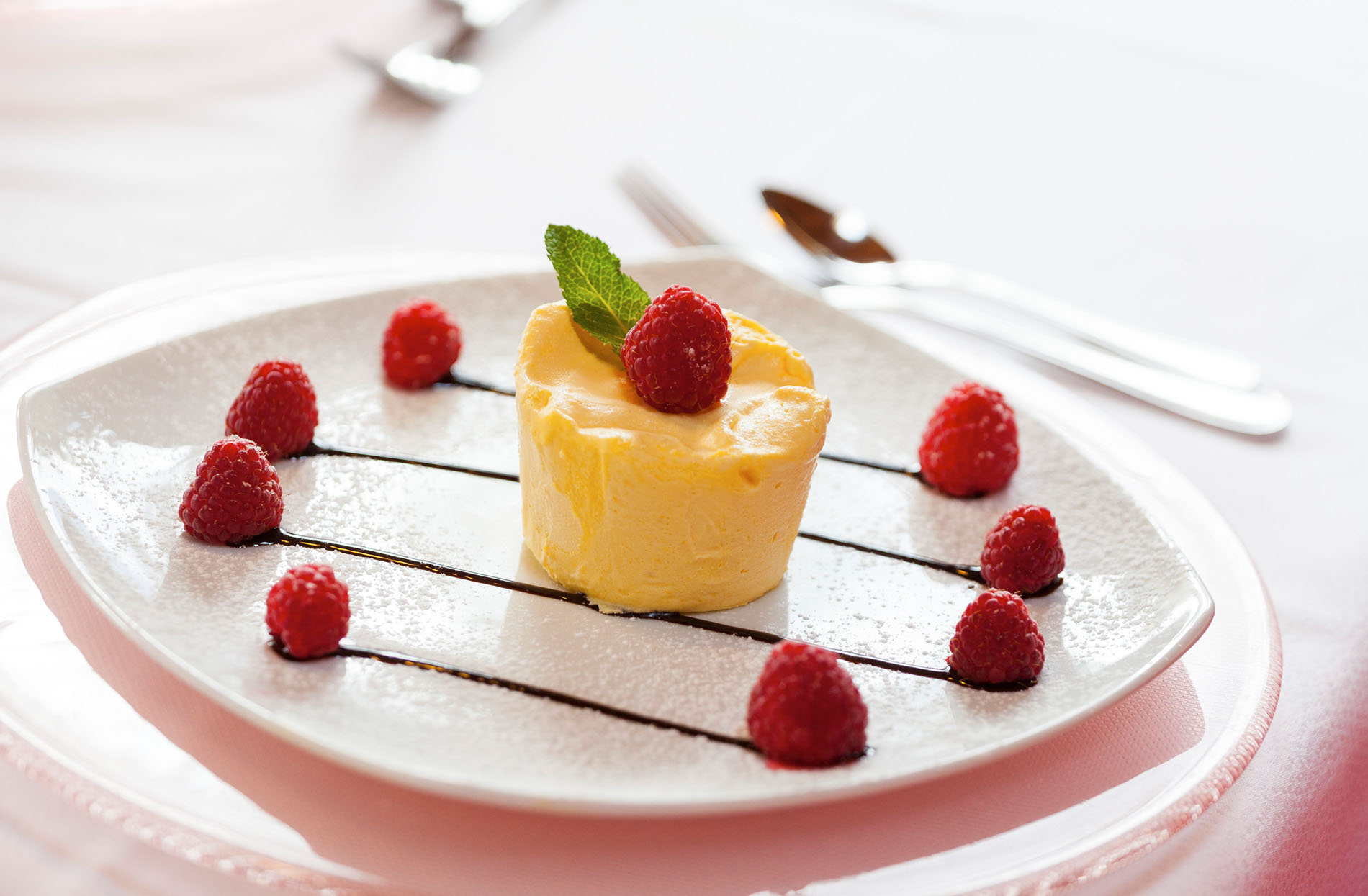 Feine Dessertportion mit Vanilleeis, Himbeeren und Minzblatt auf weißem Teller, garniert mit Schokoladensauce. Feine Dessertportion mit Vanilleeis, Himbeeren und Minzblatt auf weißem Teller, garniert mit Schokoladensauce.