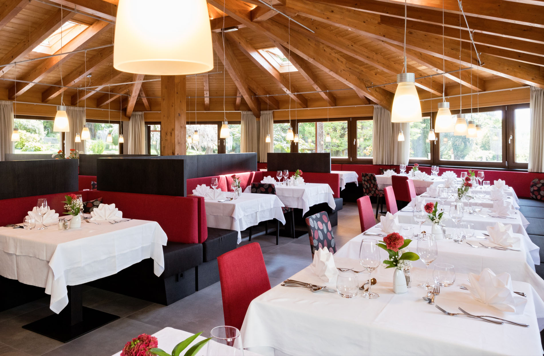 Helles Restaurant mit Holzdecke, weißen Tischdecken und rot-schwarzen Sitzbänken und Stühlen.