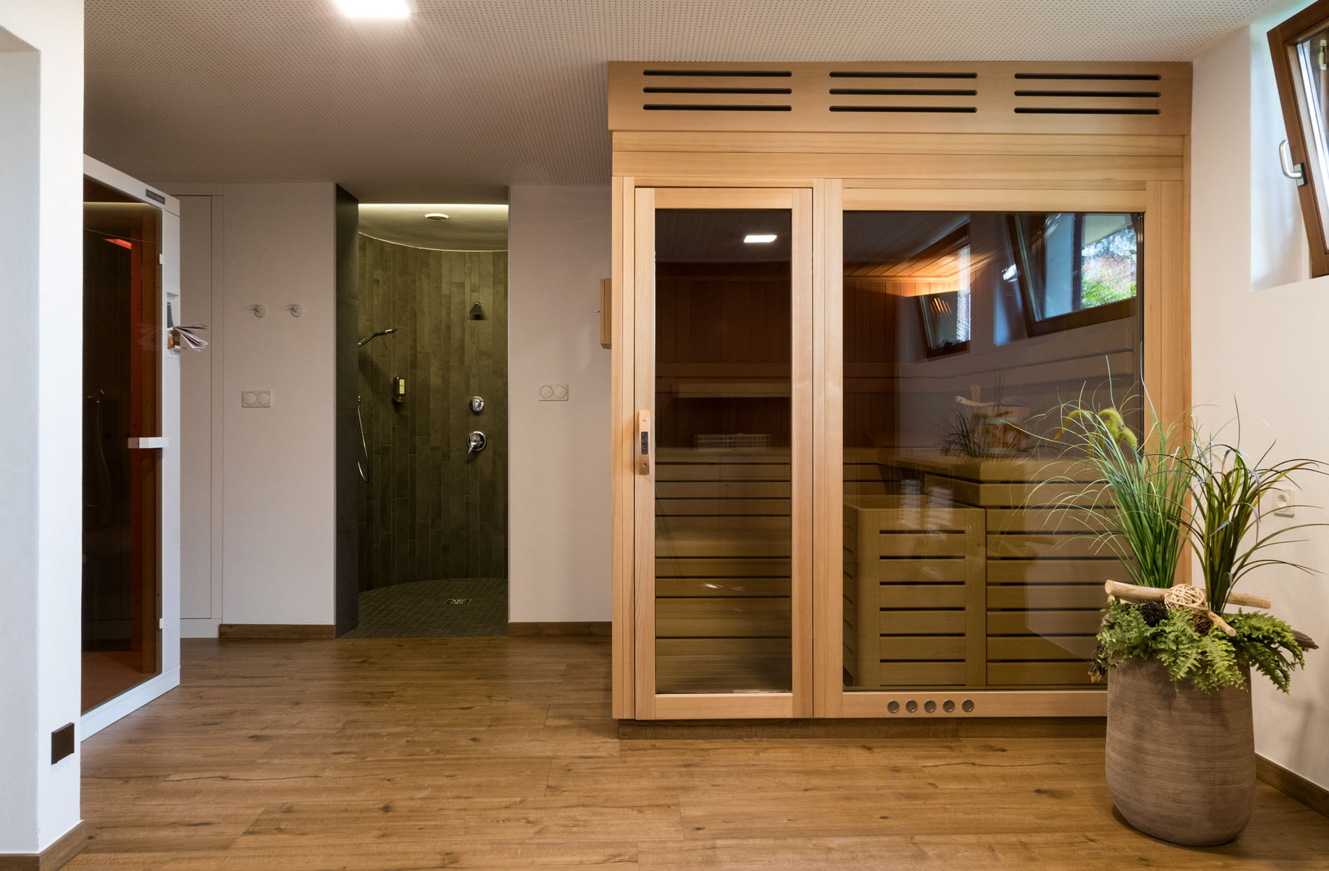Moderner Wellnessbereich mit Holzsauna, Dusche und einem Pflanzenarrangement. Moderner Wellnessbereich mit Holzsauna, Dusche und einem Pflanzenarrangement.